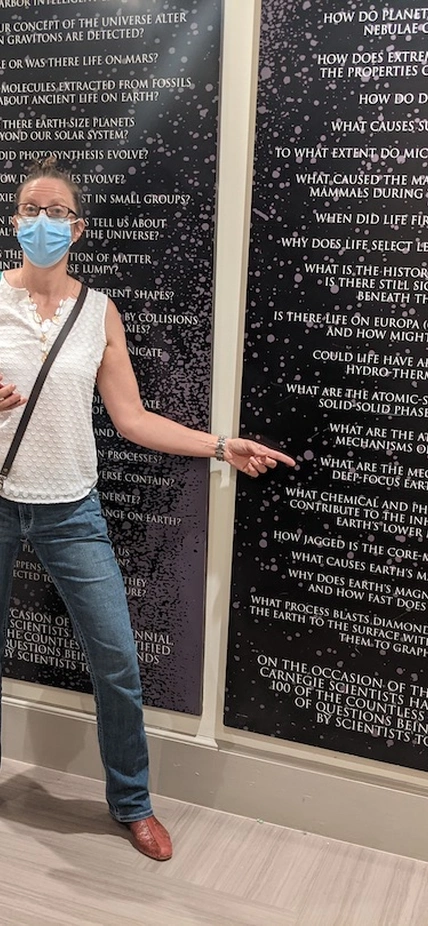 Lara Wagner points to the question, "What are the mechanisms of deep-focus earthquakes,” as a part of the top 100 questions in science display at the Carnegie Headquarters.