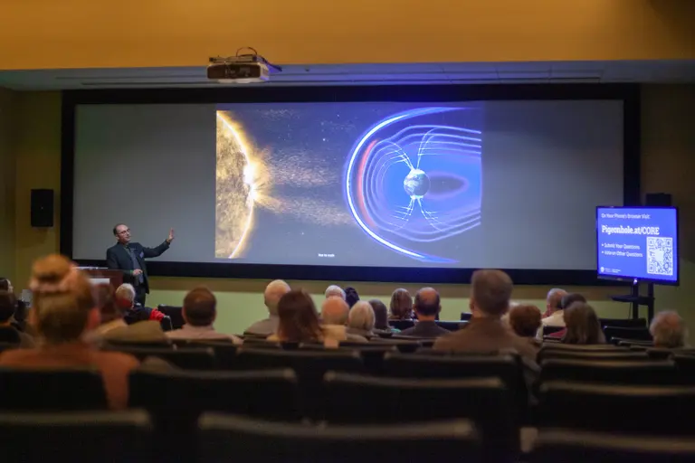 Peter Driscoll shows an image depicting how our planet's magentic field protects us from cosmic radiation to the audience at the 2023 Neighborhood Lecture Series. 