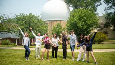 Interns cheer in front of the Atomic Physics Observatory