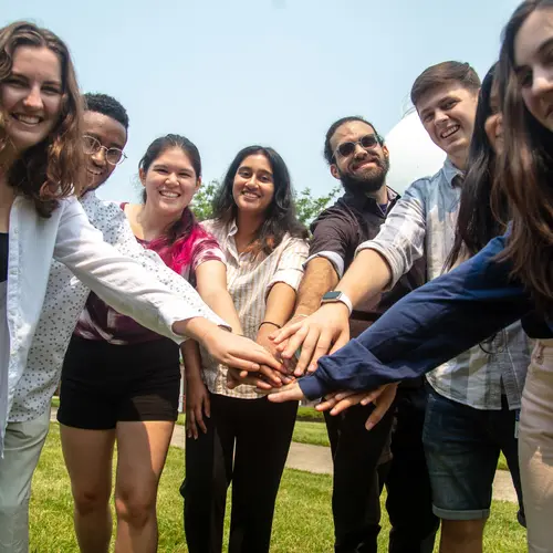 The 2023 summer interns hold their hands in the middle of the circle